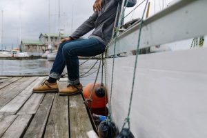 Casually dressed person sits on a wooden dock beside a boat, enjoying a peaceful day outdoors.