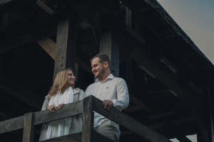 A couple smiling at each other on a wooden balcony during twilight.