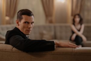 A stylish man in a suit relaxing on a sofa in an elegant room with blurred background.