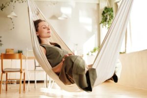 A woman enjoys a peaceful nap on an indoor hammock under soft natural light.