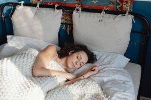 A young woman with curly hair sleeping peacefully in a cozy bed with knitted blankets.