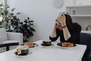 A woman sits at a table with coffee and pastries, embodying solitude and introspection indoors.