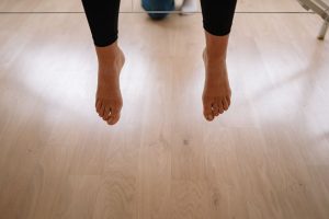 Bare feet hanging above a wooden floor indoors, creating a minimalist and warm scene.