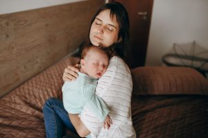A serene moment of a mother embracing her sleeping baby in a cozy bedroom setting.