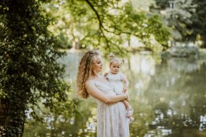 A mother affectionately holds her baby daughter in a peaceful outdoor park location.